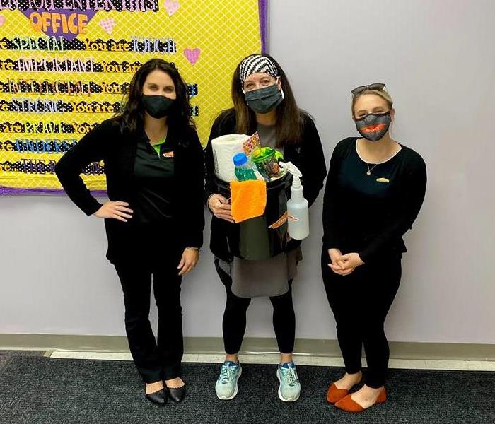 image of servpro employees with local school teacher smiling for a picture while holding a bucket of cleaning supplies