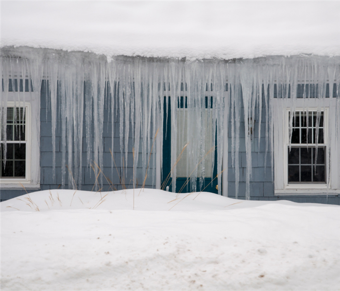 Picture shows a blue home with an exuberant amount of snow on the roof and long icicles hanging off the roof. 
